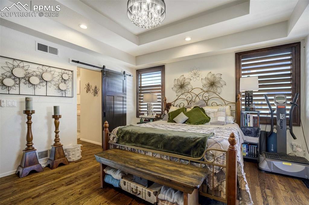 Image 21 of 50: Bedroom with a barn door, dark wood-type flooring, recessed lighting, a tra