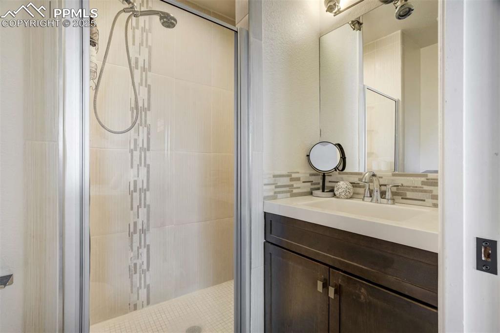 Image 27 of 50: Full bath featuring vanity, a stall shower, and decorative backsplash