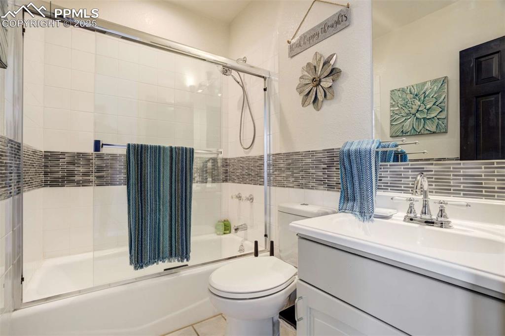Image 30 of 50: Bathroom featuring vanity, enclosed tub / shower combo, tile walls, and til