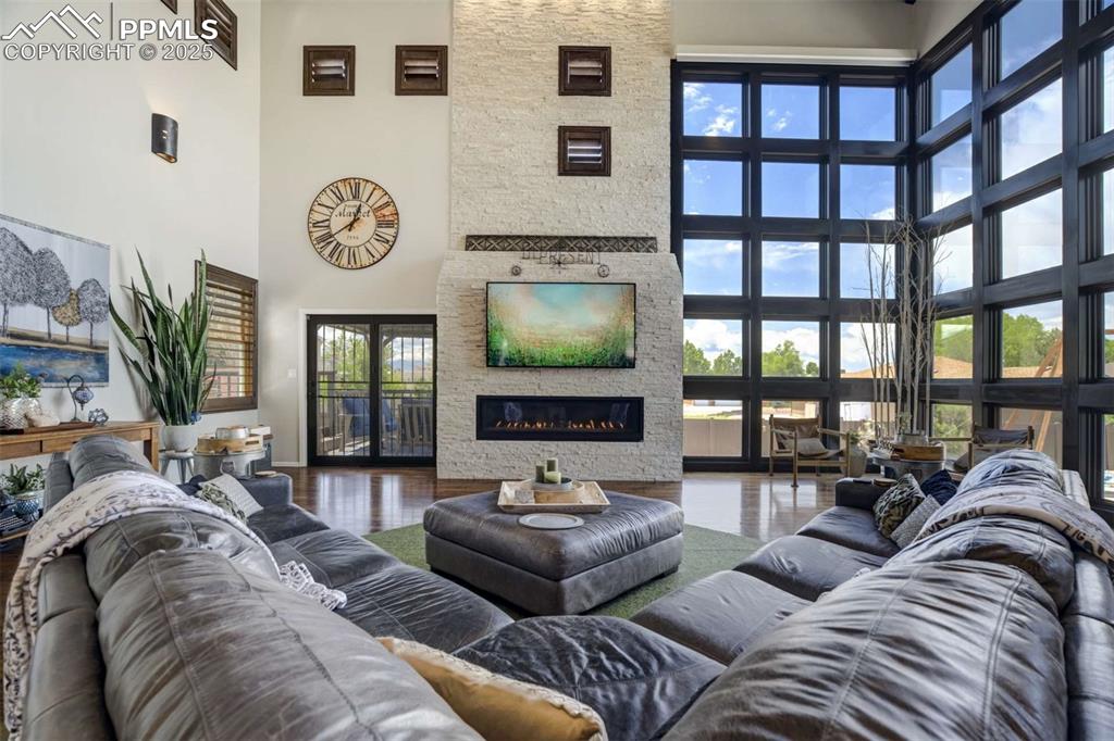 Image 4 of 50: Living area with a towering ceiling, a stone fireplace, and wood finished f