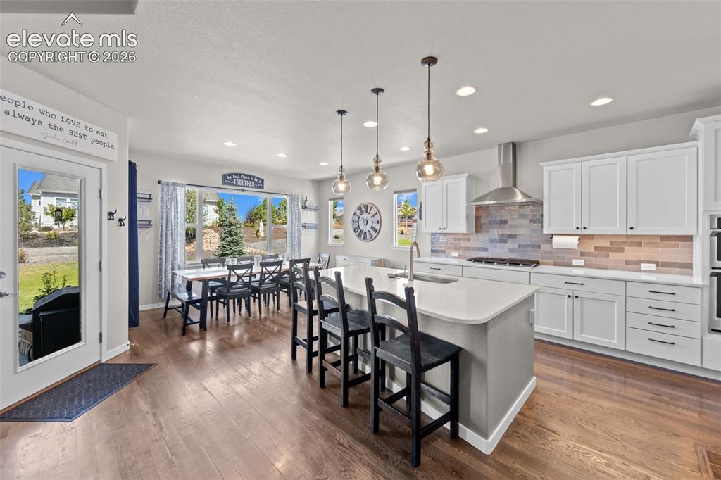 Image 10 of 32: Spacious kitchen and dining area featuring wood-finish flooring, white cabi