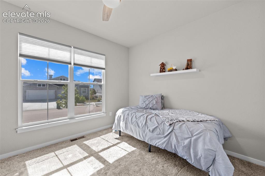 Image 8 of 32: Bright bedroom featuring a large window with pleated blinds, neutral wall p