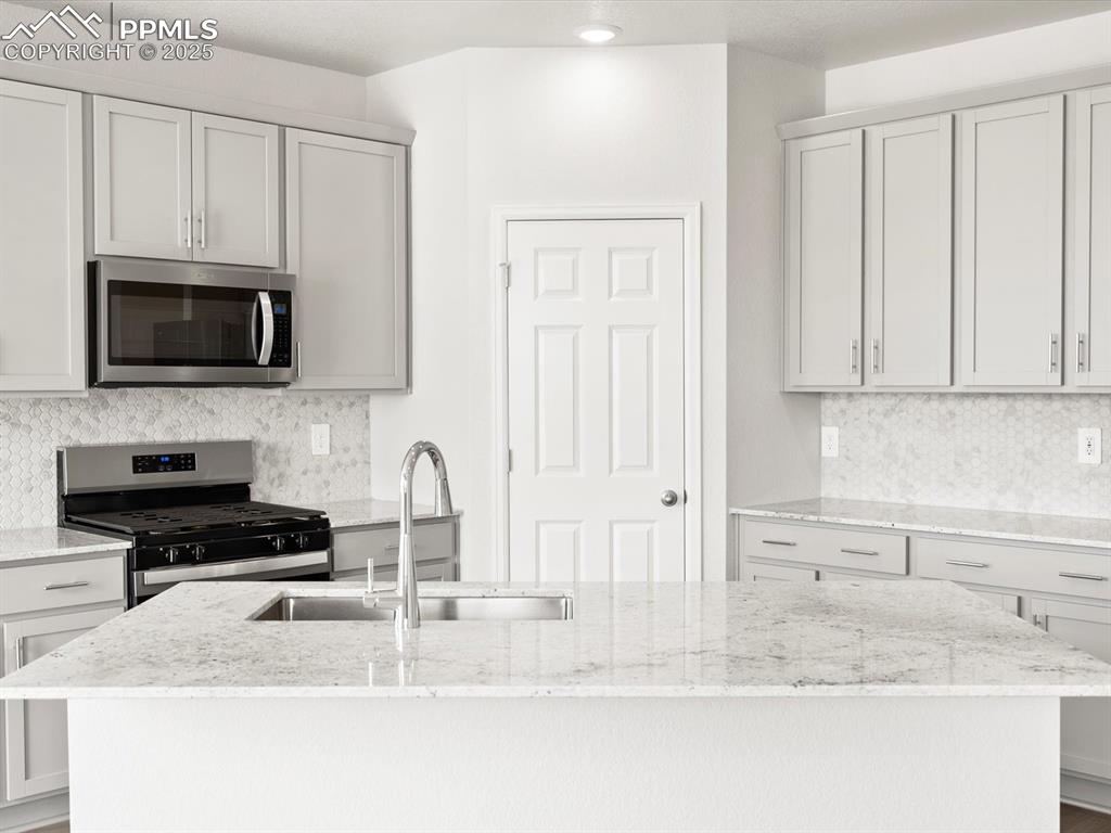 Image 3 of 19: Kitchen with tasteful backsplash, stainless steel appliances, a center isla