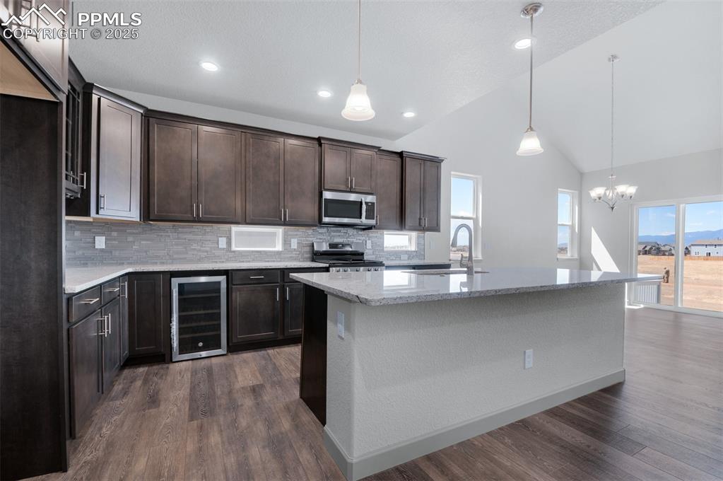 Image 5 of 21: Kitchen with dark brown cabinetry, pendant lighting, light stone countertop