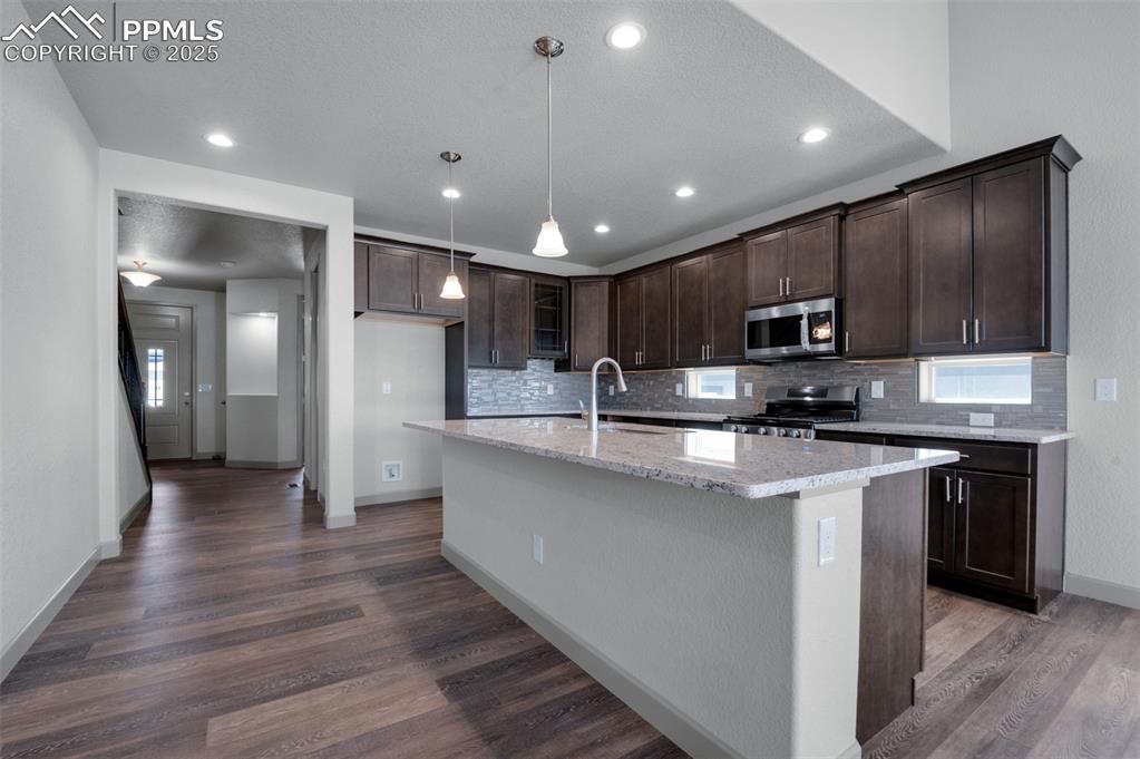 Image 6 of 21: Kitchen with dark brown cabinetry, light stone countertops, decorative back