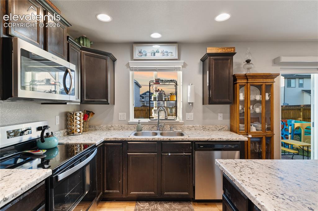 Image 18 of 43: Kitchen featuring dark wood cabinetry, light speckled countertops, and stai