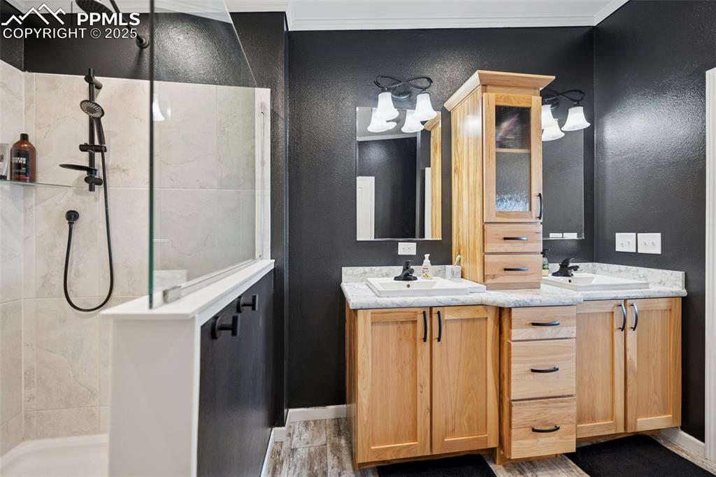 Image 25 of 34: Bathroom with double vanity, a textured wall, walk in shower, and a sink