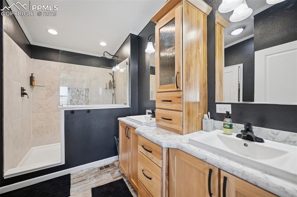 Image 26 of 34: Bathroom with double vanity, ornamental molding, a walk in shower, and a si