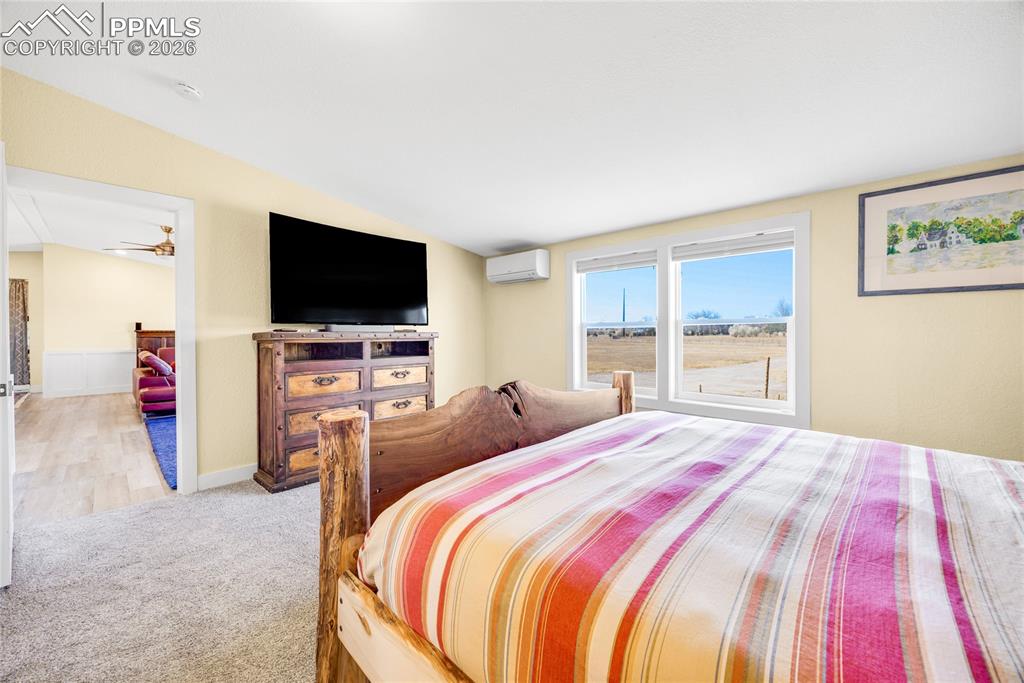 Image 19 of 49: Bedroom featuring light carpet, a wall unit AC, and lofted ceiling