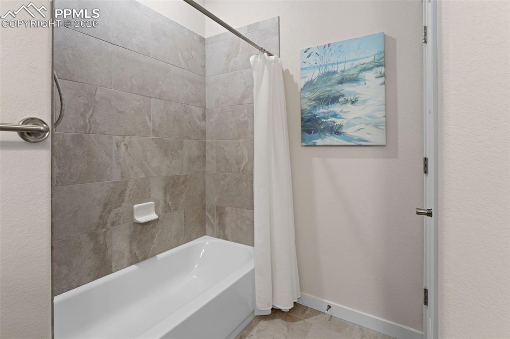 Image 28 of 42: Combo tub and shower in the second bathroom with full tile surround