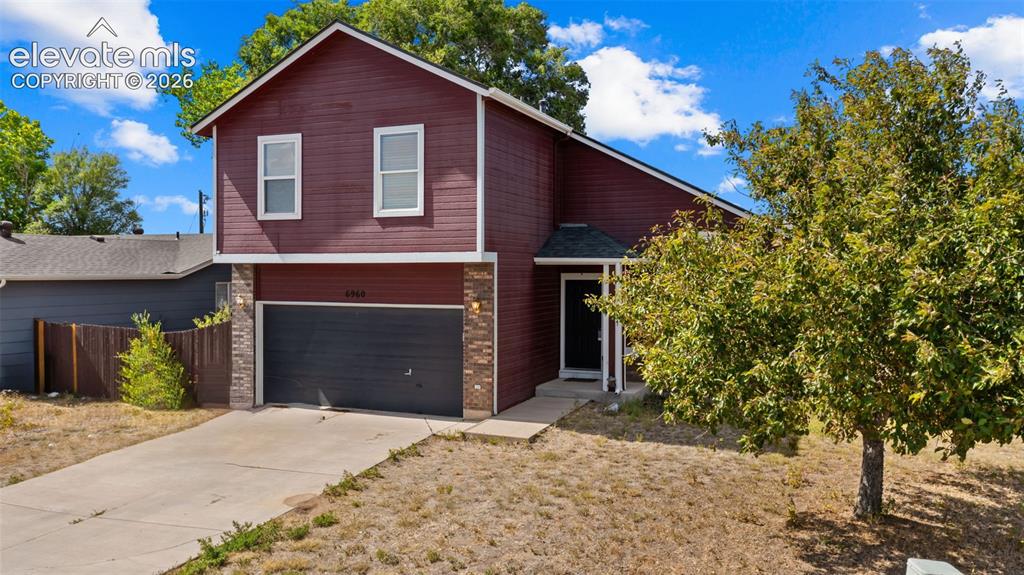 Image 3 of 33: Two-story residence featuring a two-car garage, red siding, stone accents, 