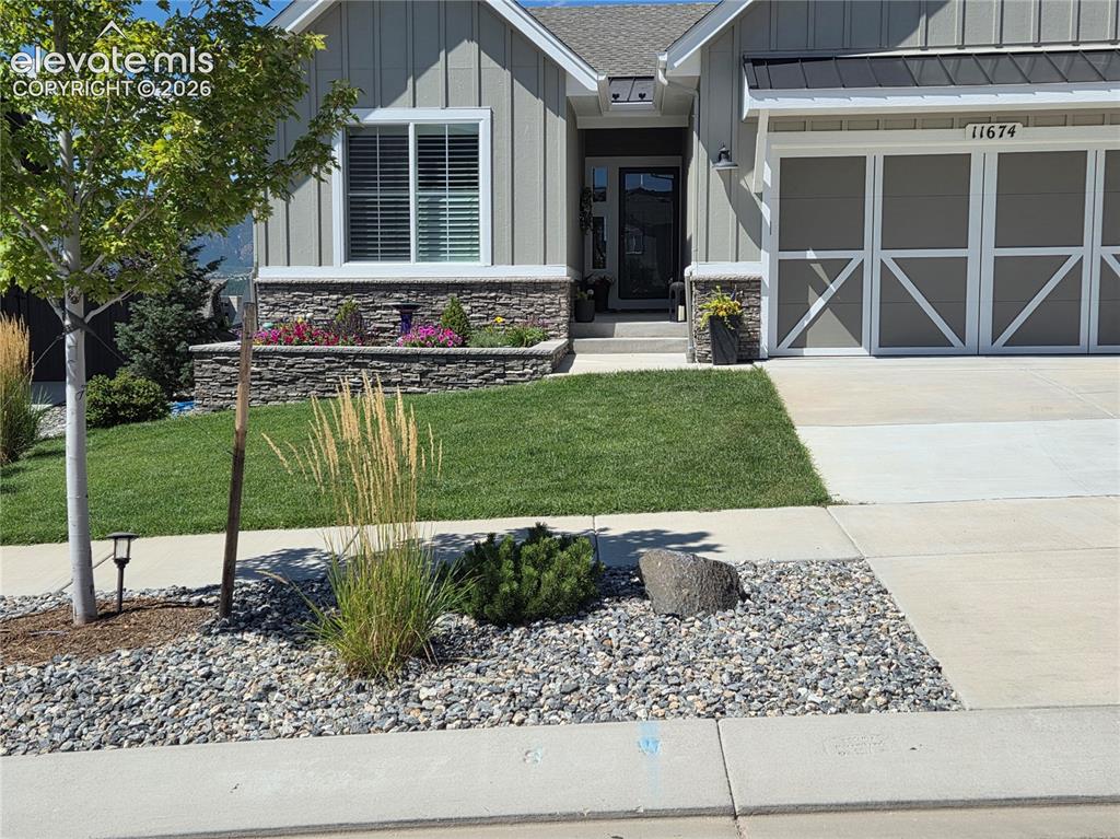 Caption: Board and batten siding with stone accents, a landscaped front yard with a retaining wall, a paved d