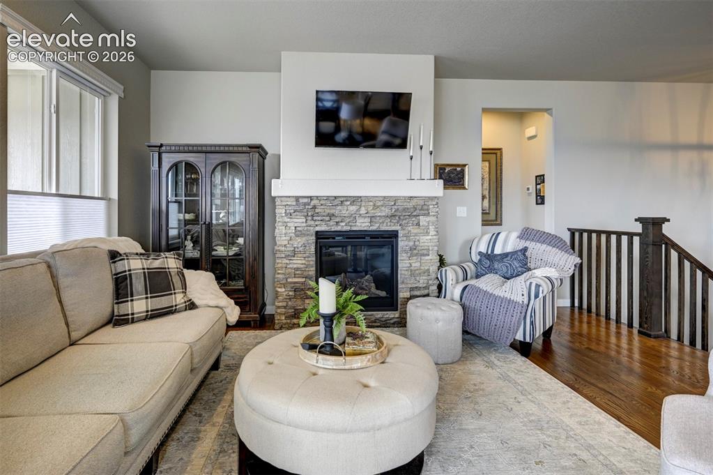 Image 12 of 29: Stone-clad fireplace with a white mantel, hardwood flooring, and a dark woo