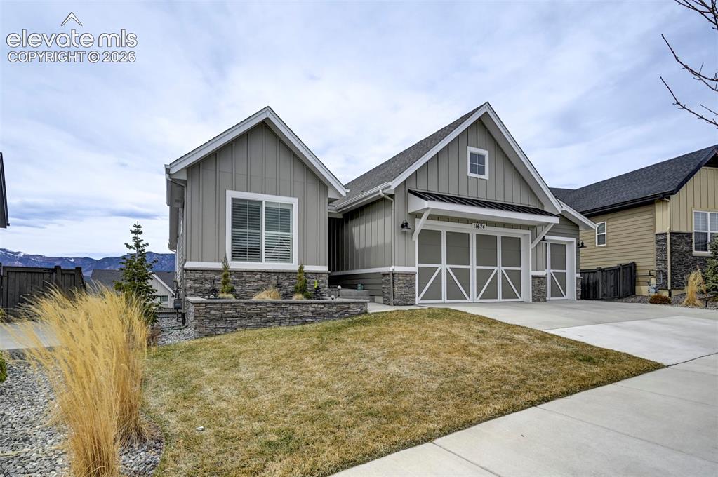 Image 2 of 29: Gable roofline, vertical panel siding, stone accent facade, two-car garage,