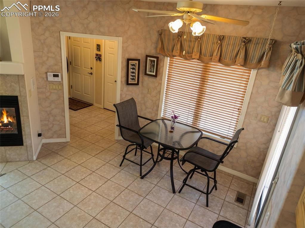 Image 11 of 30: Dining space with a tiled fireplace, a ceiling fan, light tile patterned fl