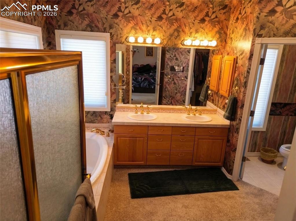 Image 17 of 30: Full bathroom with wallpapered walls, double vanity, a garden tub, light ti