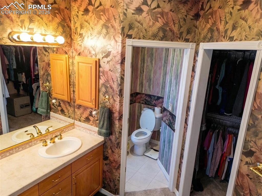 Image 18 of 30: Bathroom featuring wallpapered walls, vanity, a walk in closet, and light t