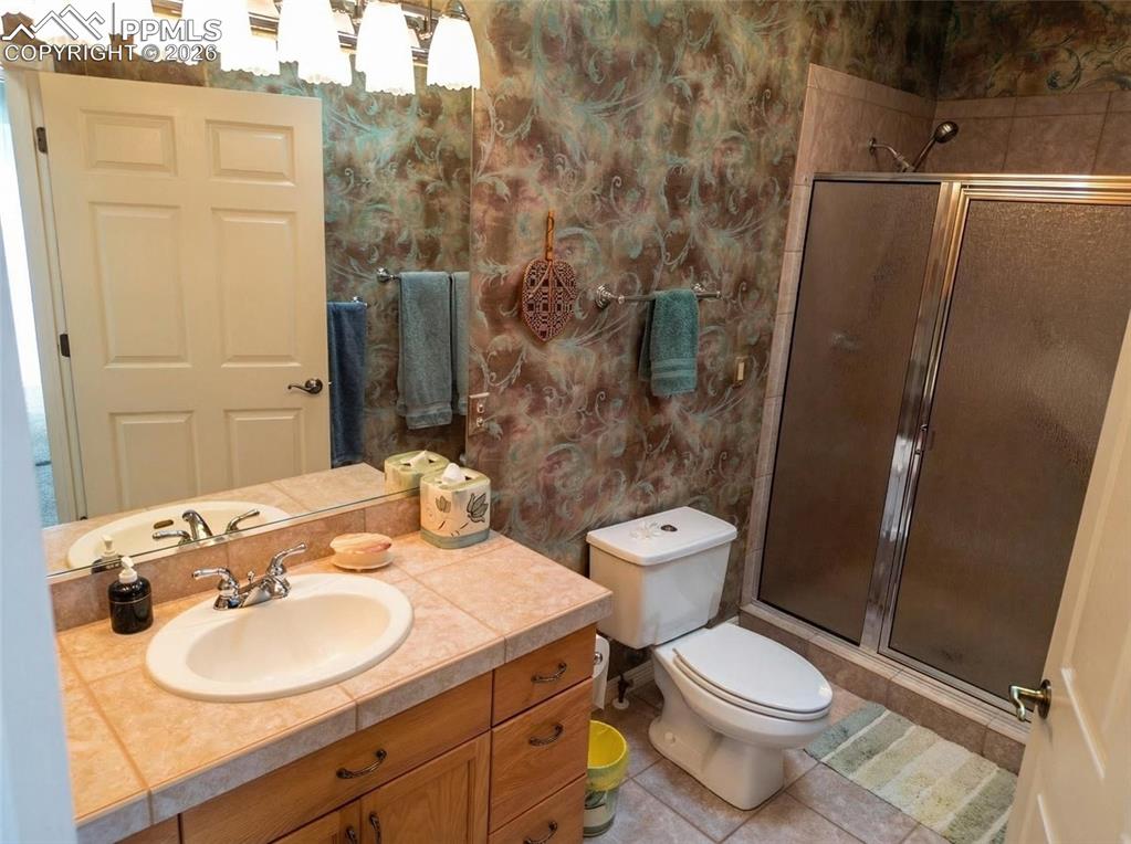 Image 20 of 30: Bathroom featuring a stall shower, vanity, wallpapered walls, and light til