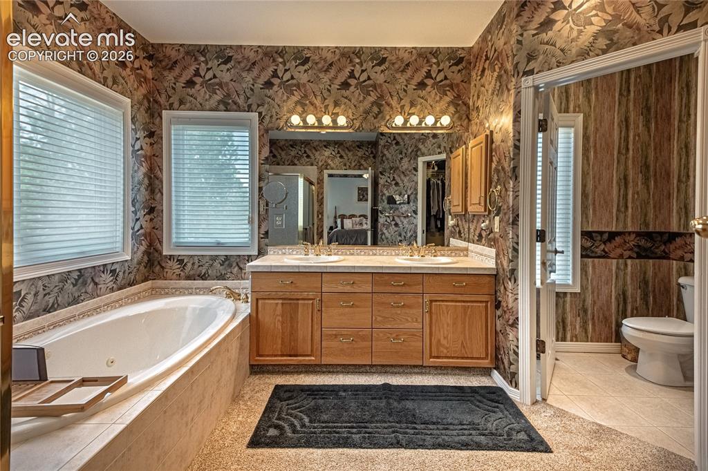 Image 32 of 50: Bathroom featuring a jetted soaking tub, dual windows with blinds, a double