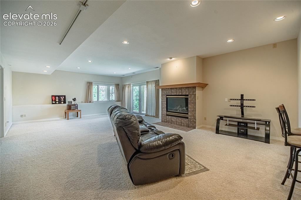 Image 40 of 50: Spacious lower-level room featuring a tiled fireplace with wood mantel, rec