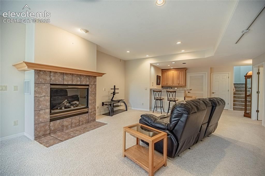 Image 42 of 50: Carpeted living area featuring a stone tile fireplace with a wood mantel