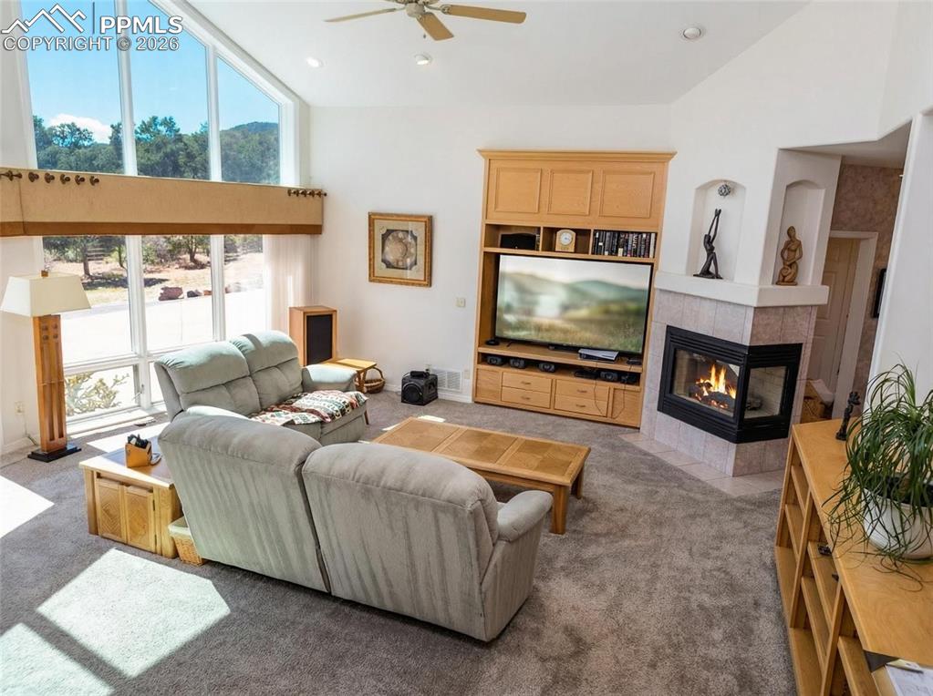 Image 5 of 30: Living room with lofted ceiling, a ceiling fan, a tiled fireplace, carpet f