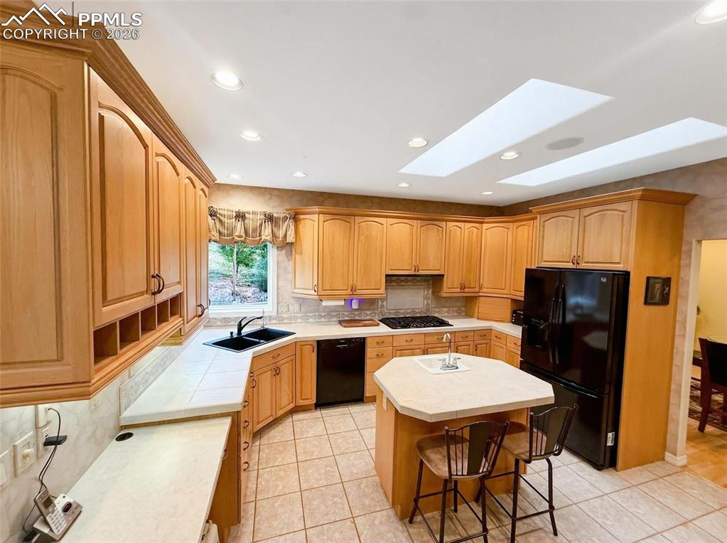 Image 7 of 30: Kitchen with black appliances, double skylights, a breakfast bar, decorativ