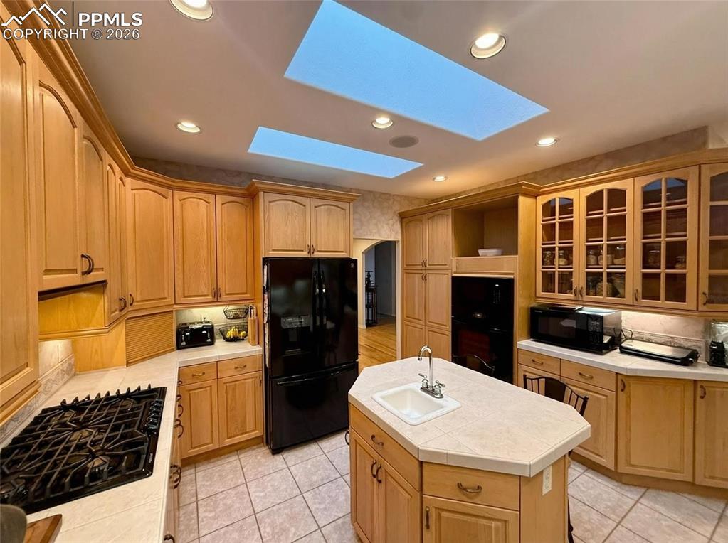 Image 8 of 30: Kitchen with black appliances, a kitchen island with sink, tile counters, g