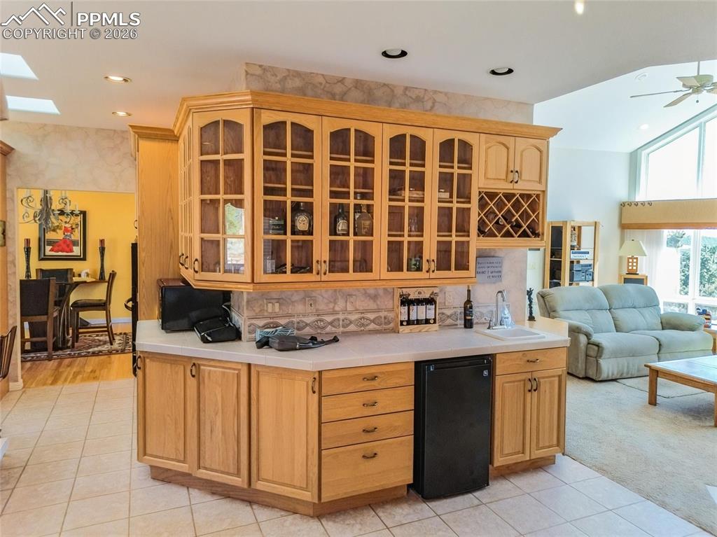 Image 9 of 30: Kitchen with open floor plan, glass fronted cabinets, ceiling fan, light ti