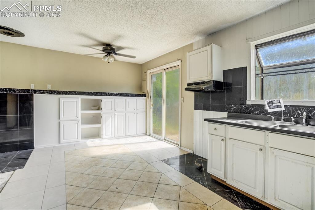 Image 7 of 24: Kitchen with white cabinets, light tile patterned floors, dark countertops,