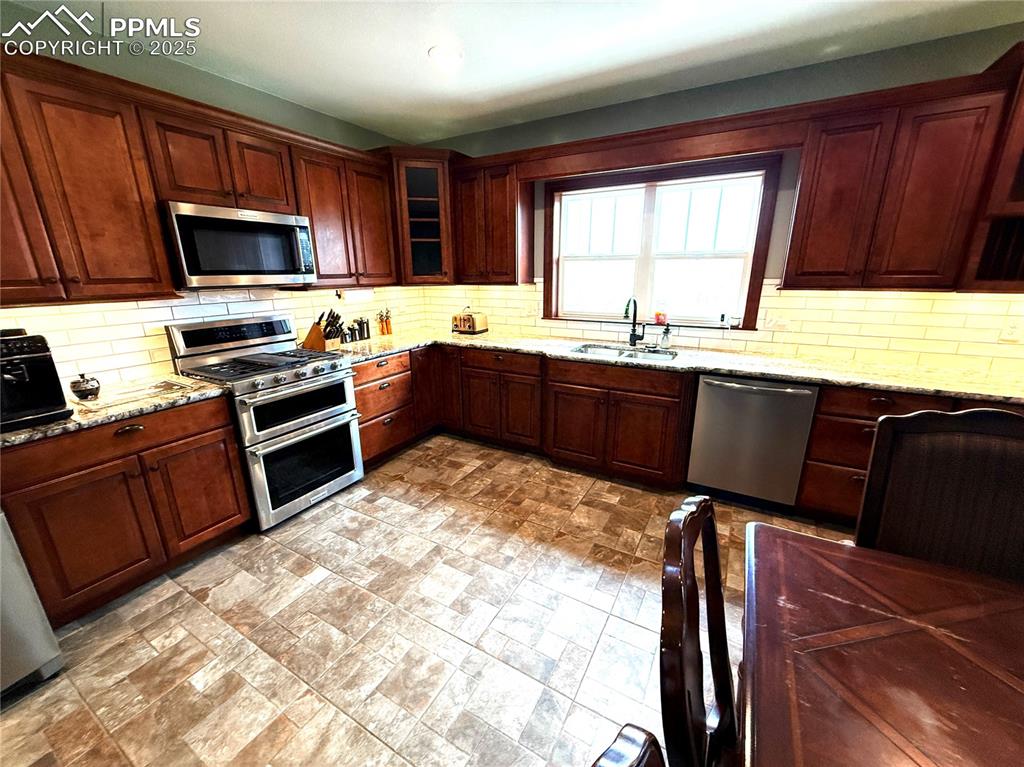 Image 6 of 50: Kitchen featuring light stone countertops, stainless steel appliances, deco