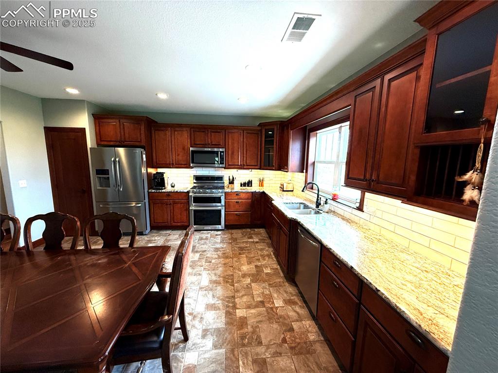 Image 7 of 50: Kitchen with backsplash, appliances with stainless steel finishes, glass in