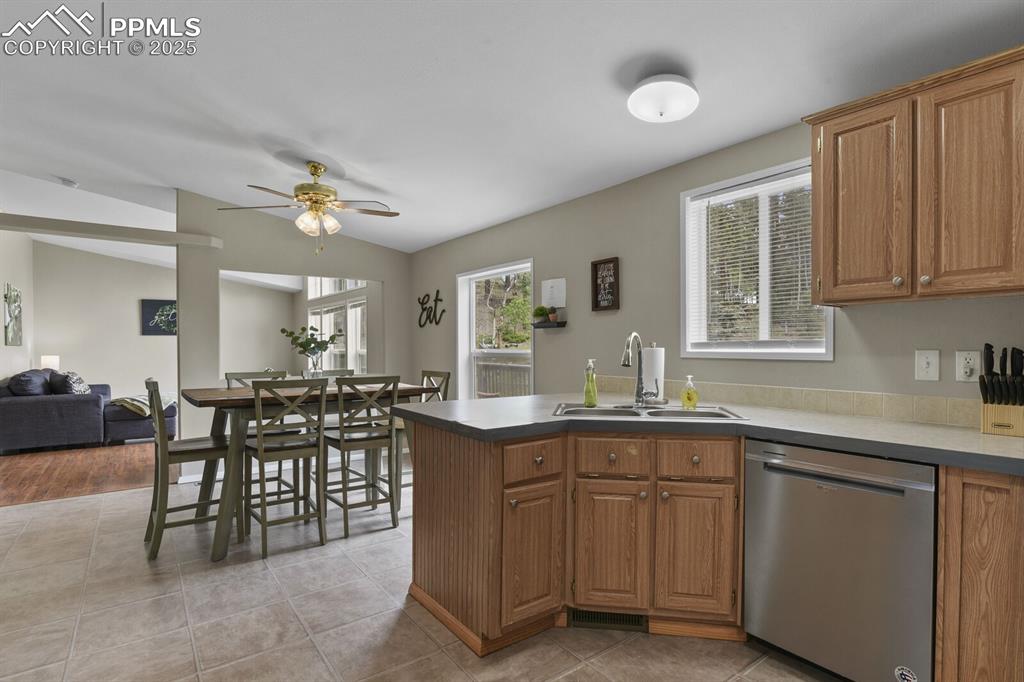 Image 13 of 37: Kitchen featuring dishwasher, a peninsula, brown cabinetry, light tile patt