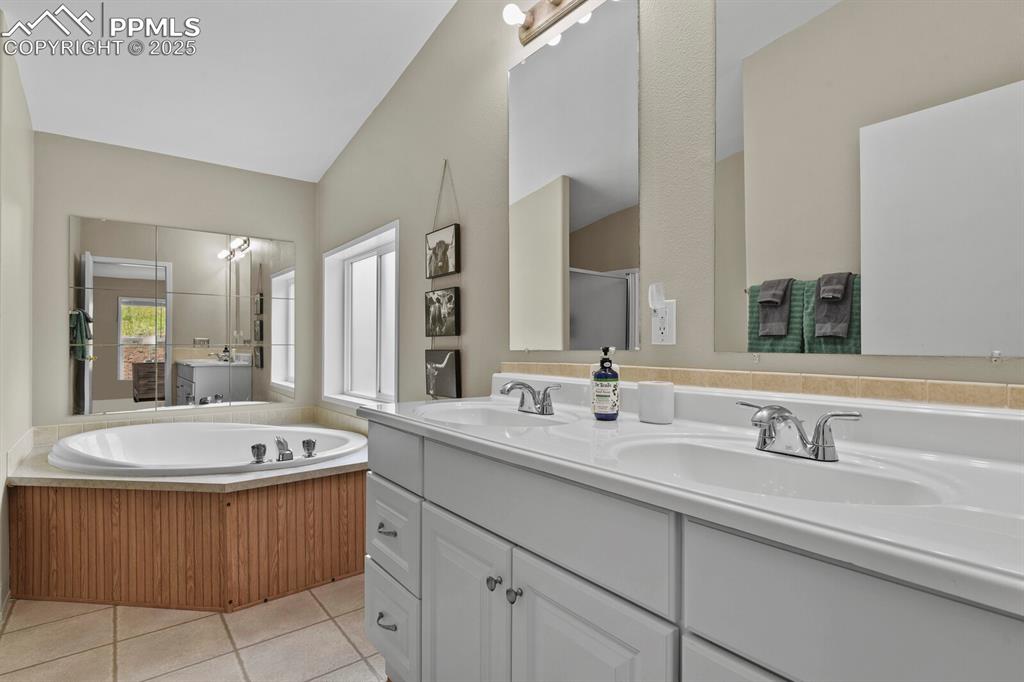 Image 16 of 37: Bathroom with double vanity, a garden tub, light tile patterned floors, and
