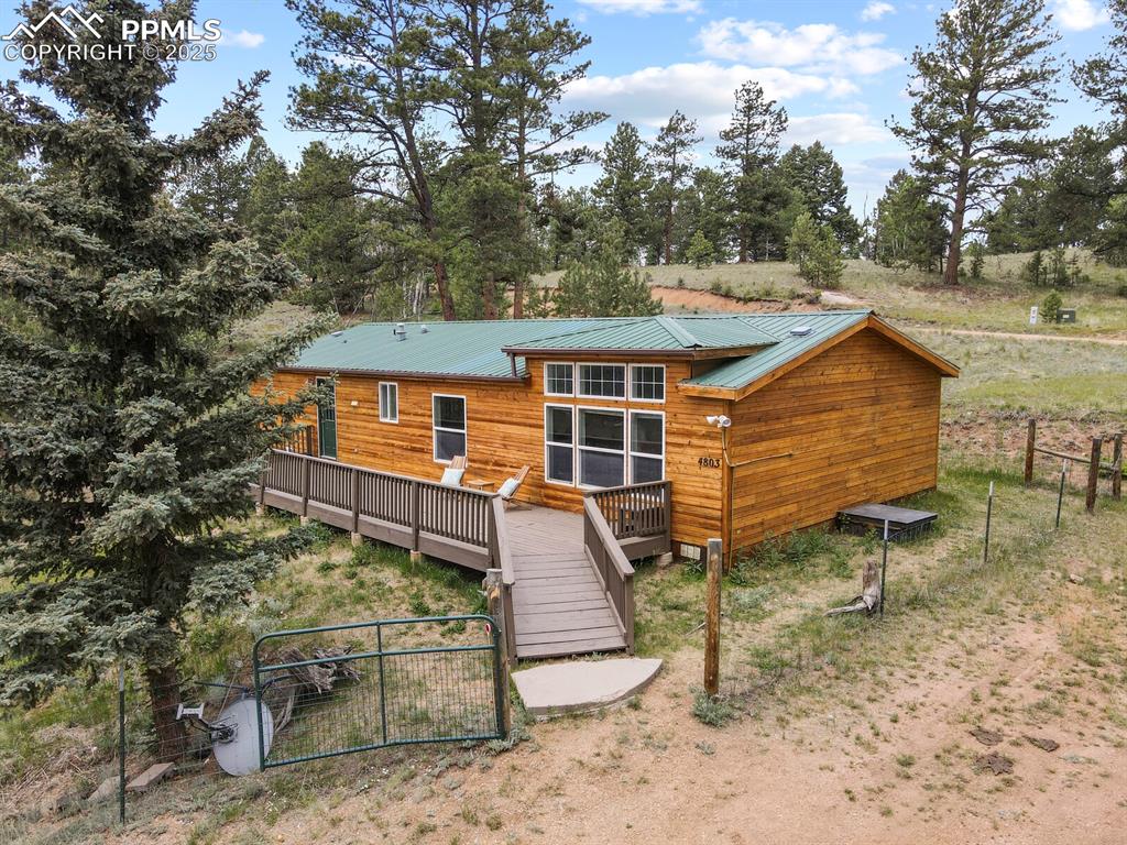 Image 29 of 37: Back of house featuring a deck, a gate, a metal roof, and view of wooded ar