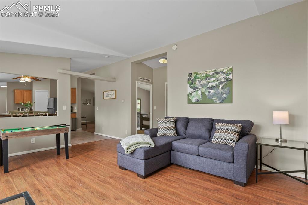 Image 6 of 37: Living room with light wood finished floors, a ceiling fan, and vaulted cei