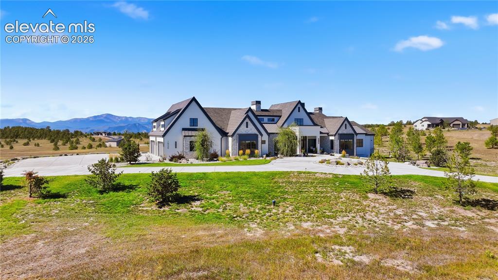 Image 3 of 50: Multi-gabled estate featuring stone and masonry exterior, expansive concret