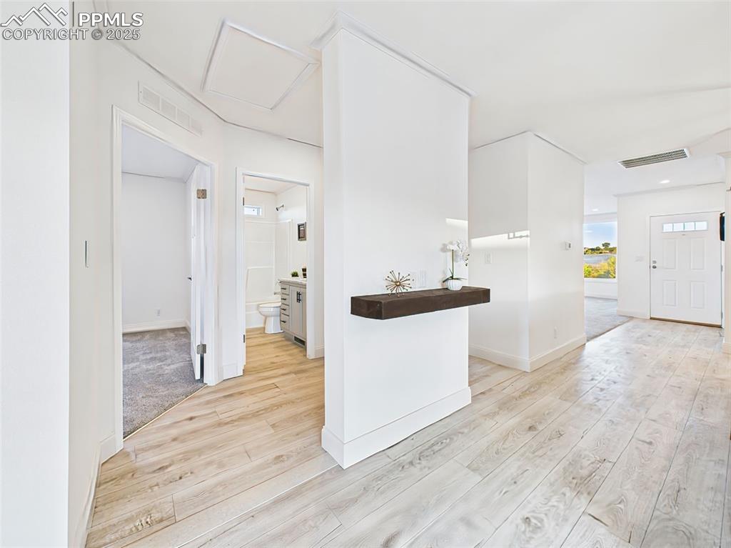 Image 33 of 50: Open hallway with light wood flooring leading to guest rooms and bath.