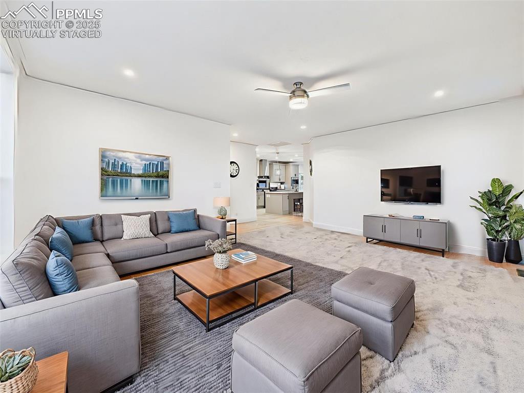 Image 9 of 50: Virtually Staged Living room with ceiling fan looking into kitchen