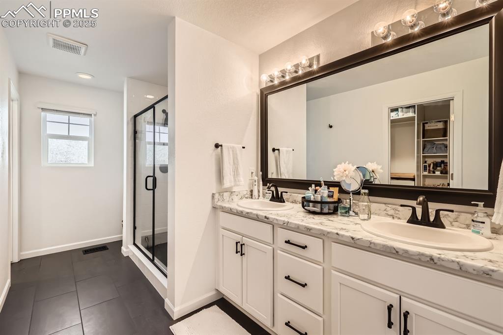 Image 22 of 28: Full bathroom with double vanity, a stall shower, and tile patterned floori