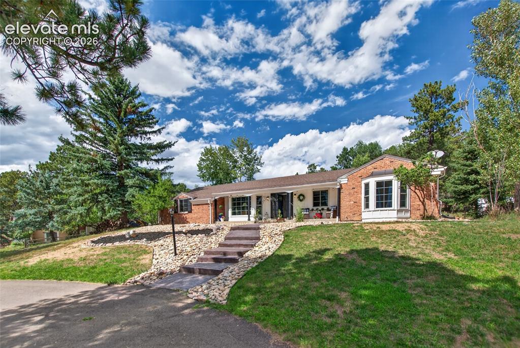 Image 2 of 43: Brick exterior with a prominent bay window, stone-edged terraced landscapin