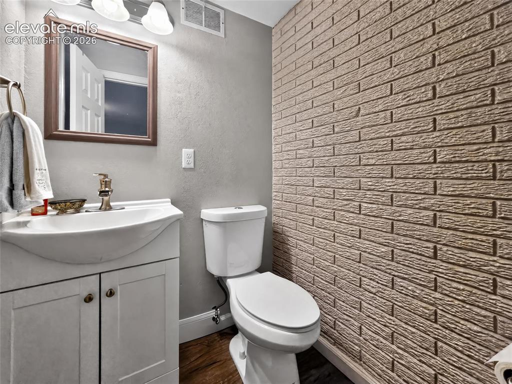 Image 26 of 43: Textured brick-style accent wall, wood-finish flooring, white vanity with i