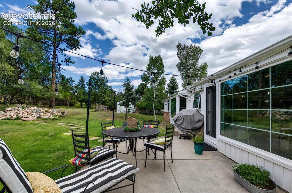 Image 28 of 43: Expansive concrete patio with large pane windows, and a lush green lawn sur