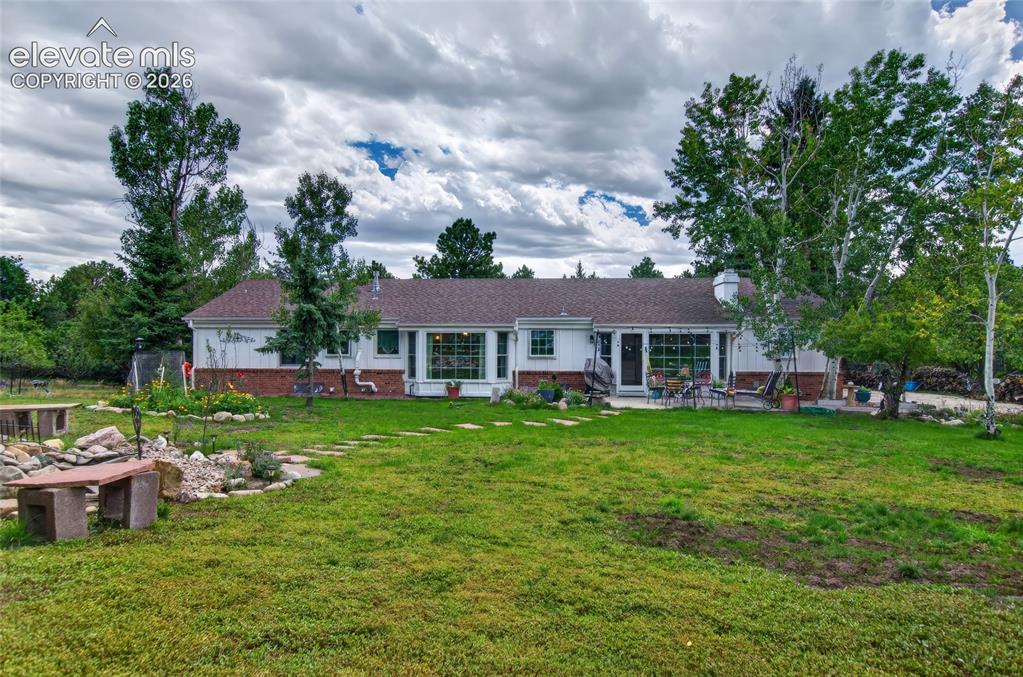 Image 31 of 43: Expansive lawn with a stone pathway, mature trees, and a ground-level patio