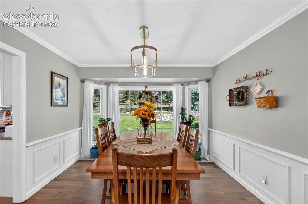 Image 7 of 43: Bay window overlooking the yard, wood-finish flooring, wainscoting, crown m