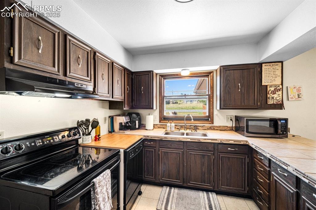 Image 10 of 38: Kitchen with black appliances, dark brown cabinets, under cabinet range hoo