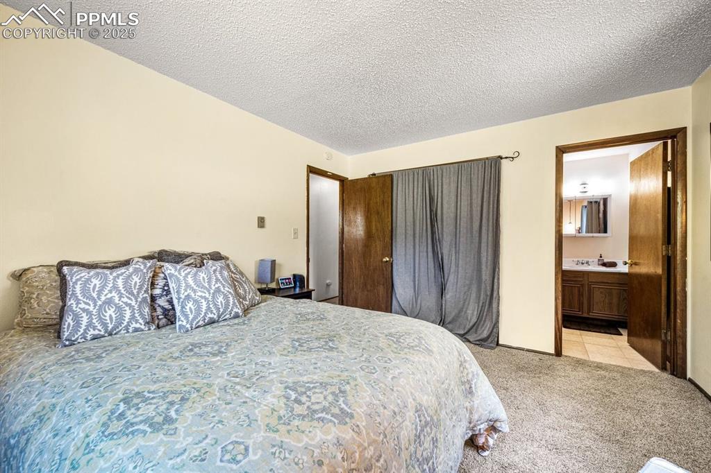 Image 22 of 38: Bedroom with light carpet, a textured ceiling, and ensuite bathroom
