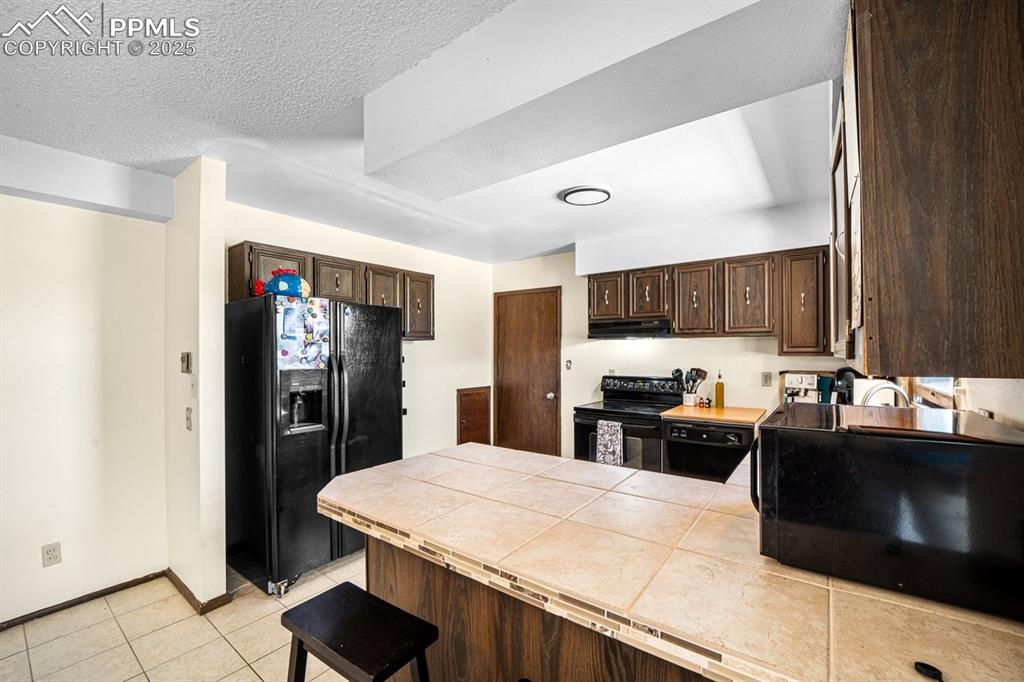 Image 9 of 38: Kitchen featuring dark brown cabinets, black appliances, light tile pattern