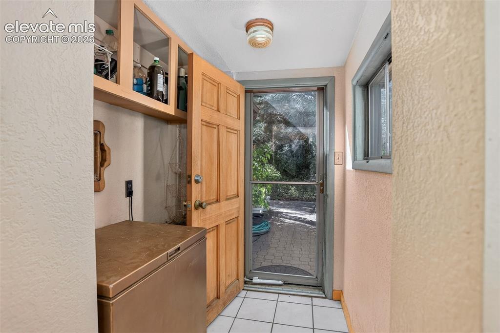 Image 18 of 25: Wood-panel door, white tile flooring, built-in upper cabinetry, and a windo