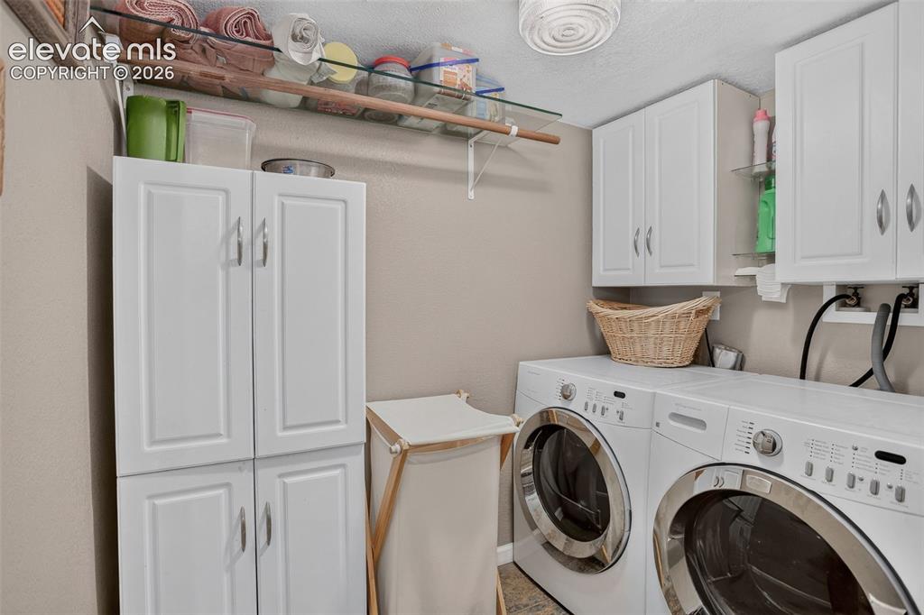 Image 23 of 25: Dedicated laundry space with built-in white cabinetry, glass shelving, and
